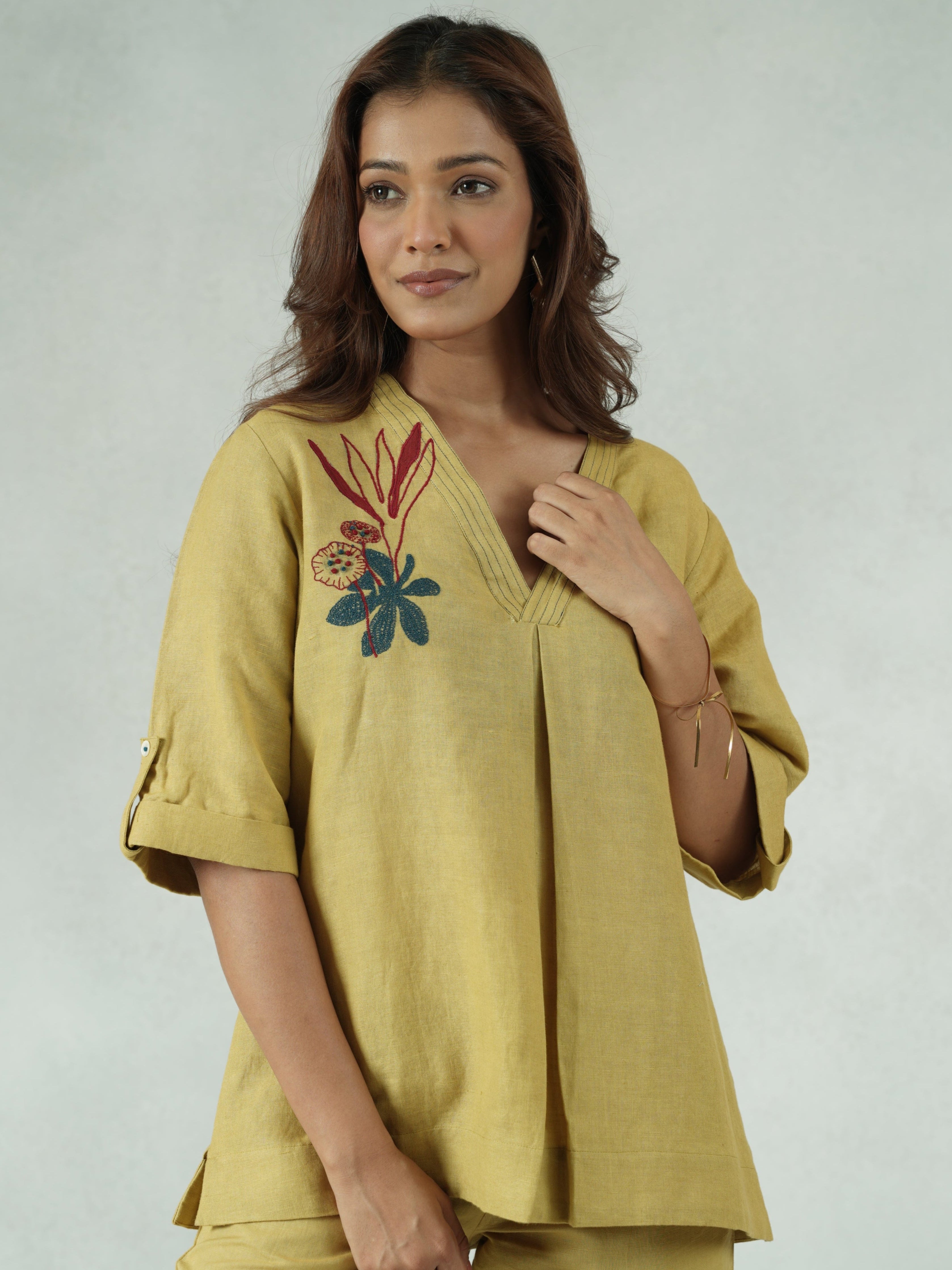 Woman wearing a yellow outfit with floral embroidery on a plain background