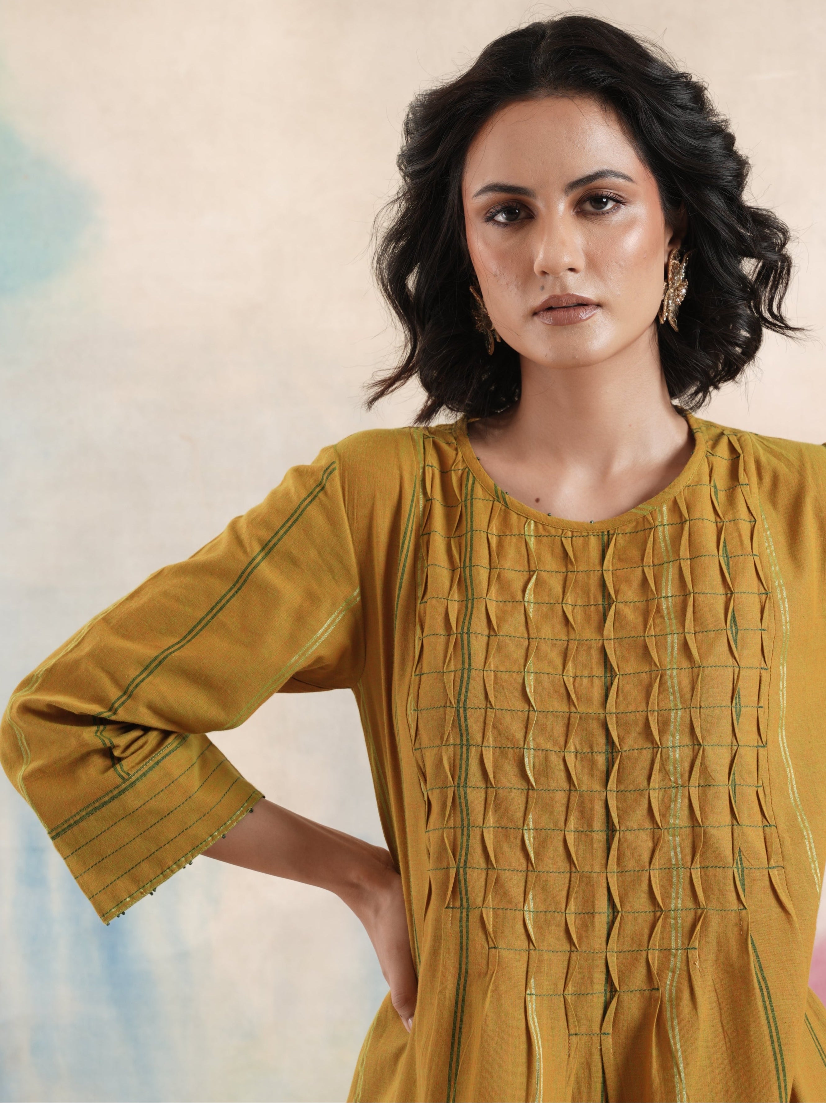 Woman in a mustard yellow dress with textured pattern against a pastel background.