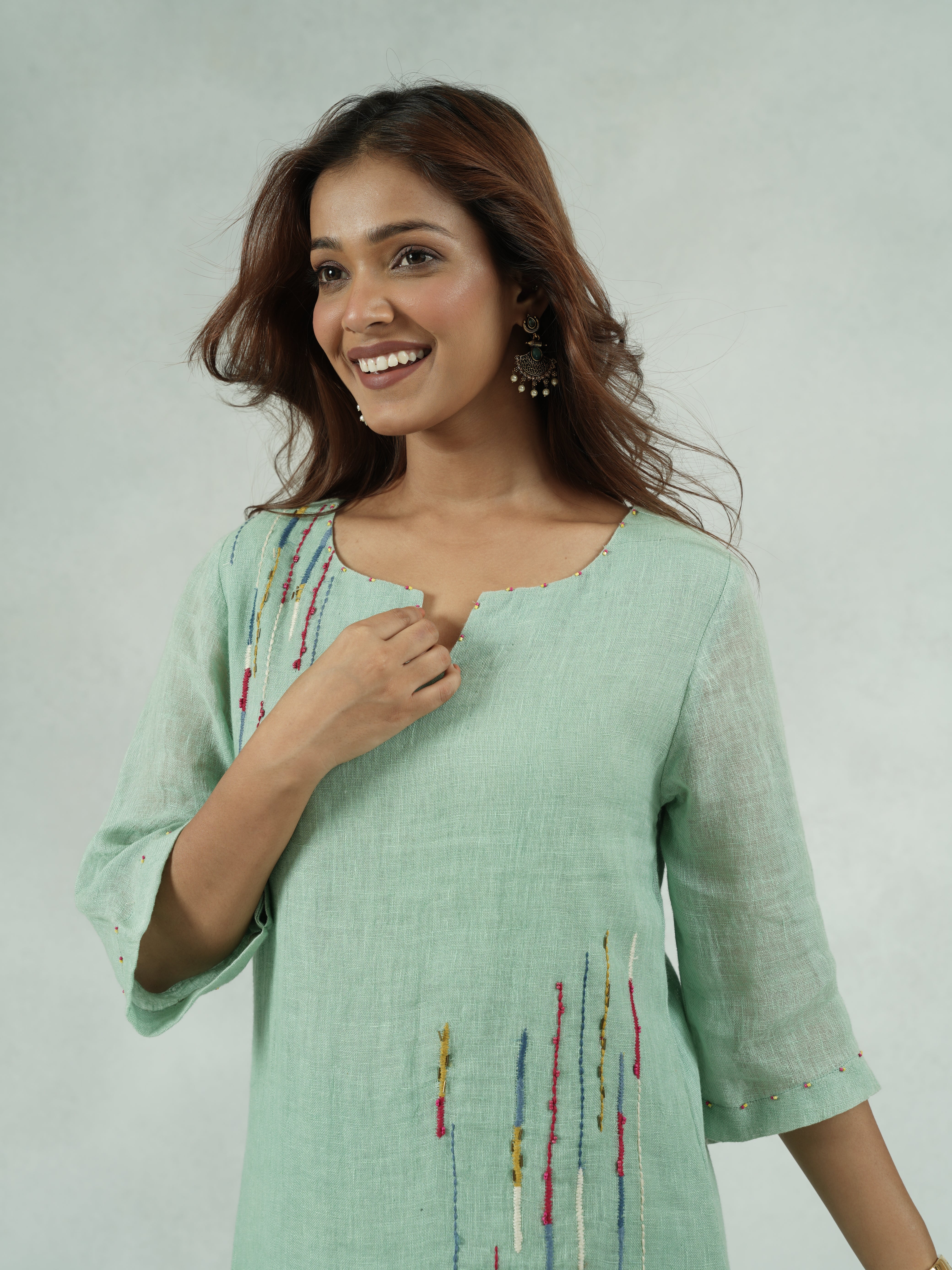 Woman wearing a light green dress with colorful embroidery on a white background