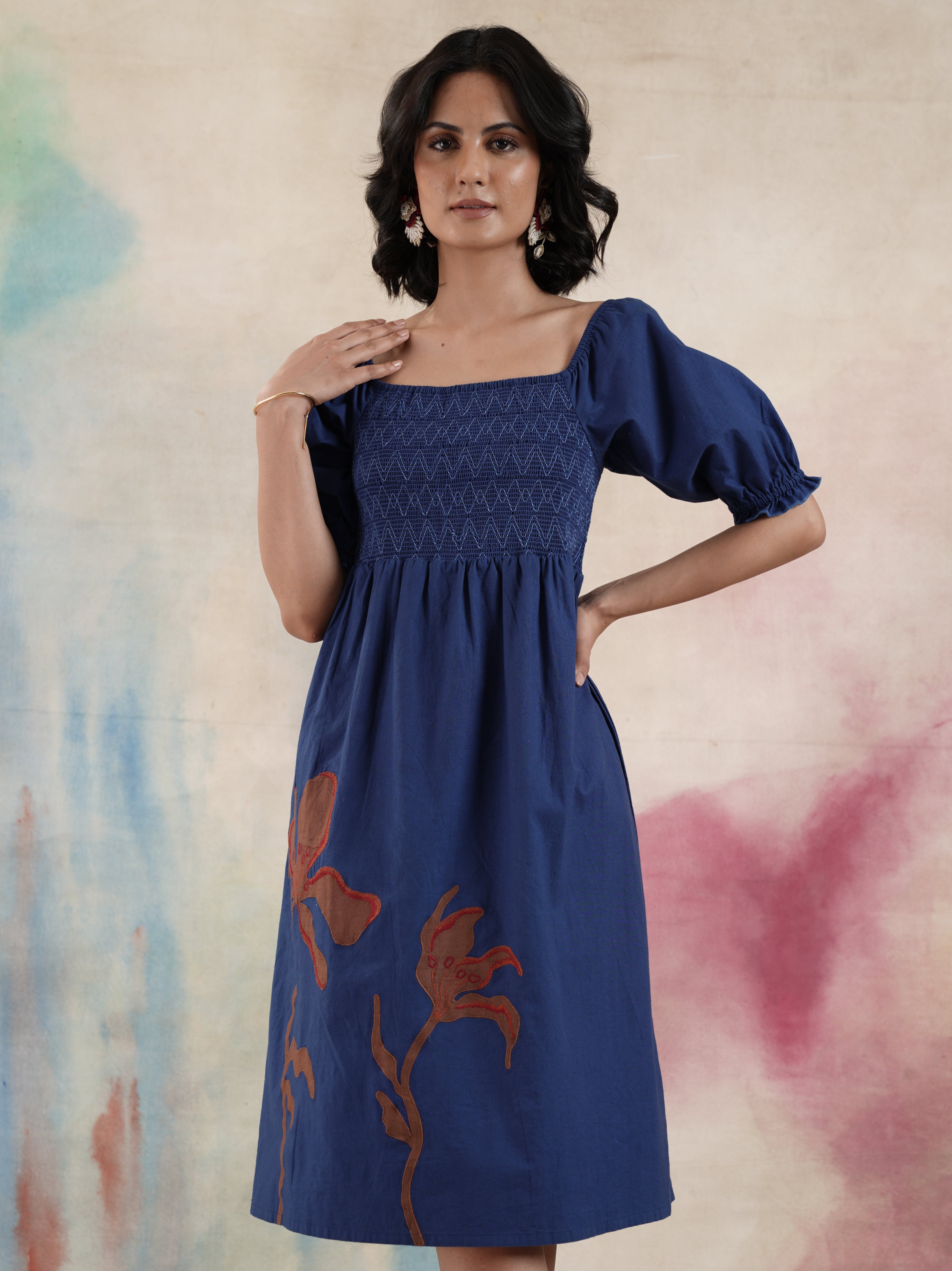 A woman modeling a navy blue cotton ankle-length dress with balloon sleeves and palm leaf applique detailing.