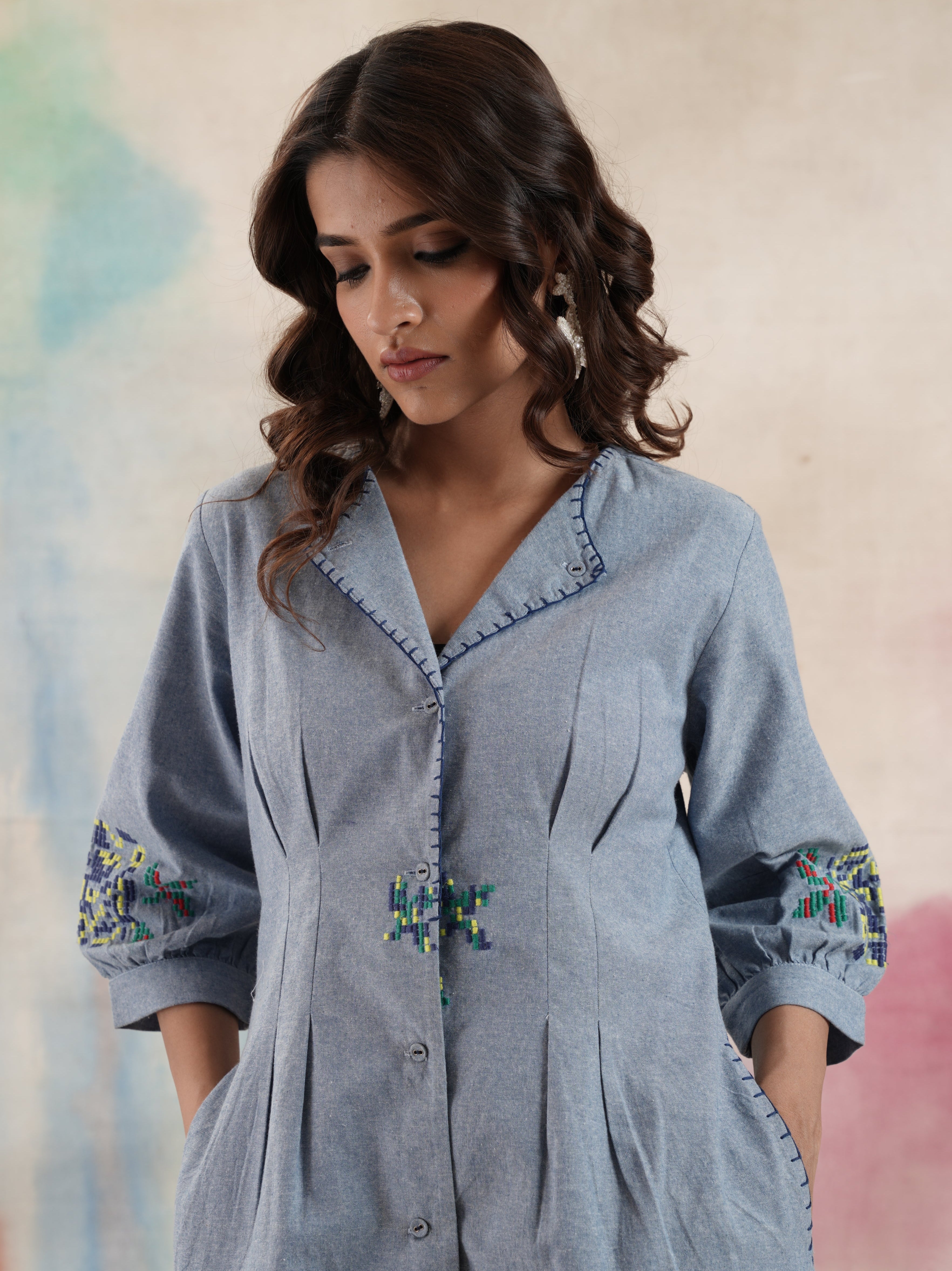 Woman wearing a light blue denim shirt with embroidered details on a colorful background.