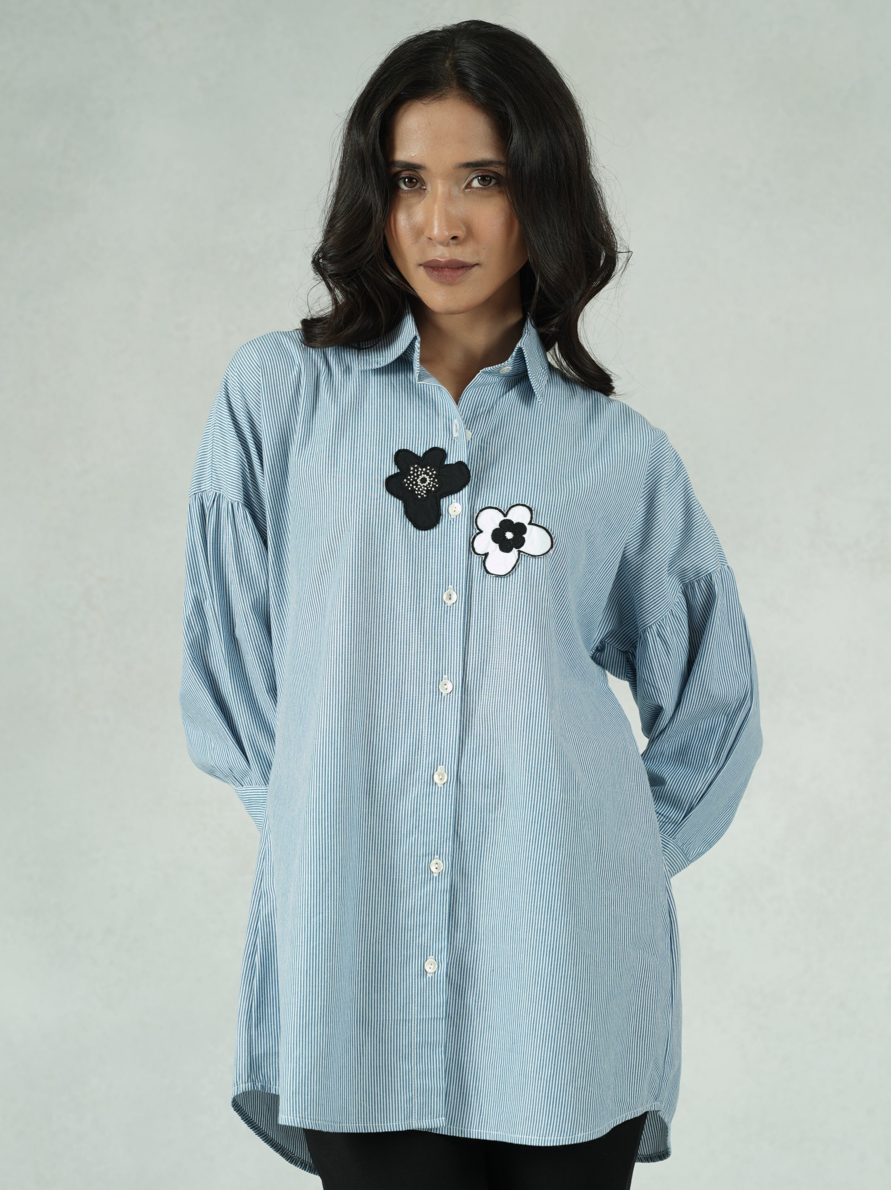 Person wearing a light blue shirt with a black flower design on a gray background
