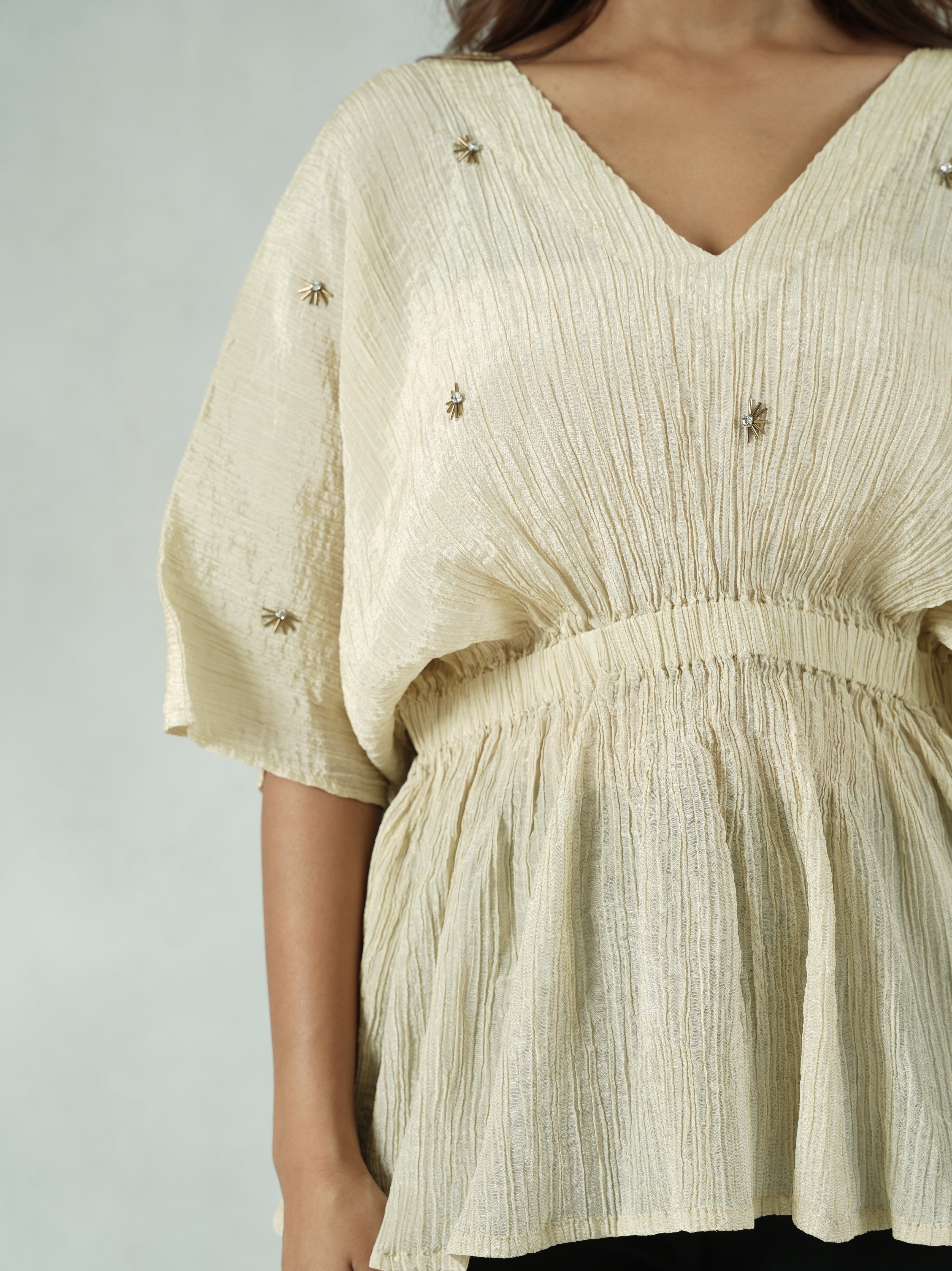 Close-up of a person wearing a cream-colored outfit with intricate detailing on a plain background