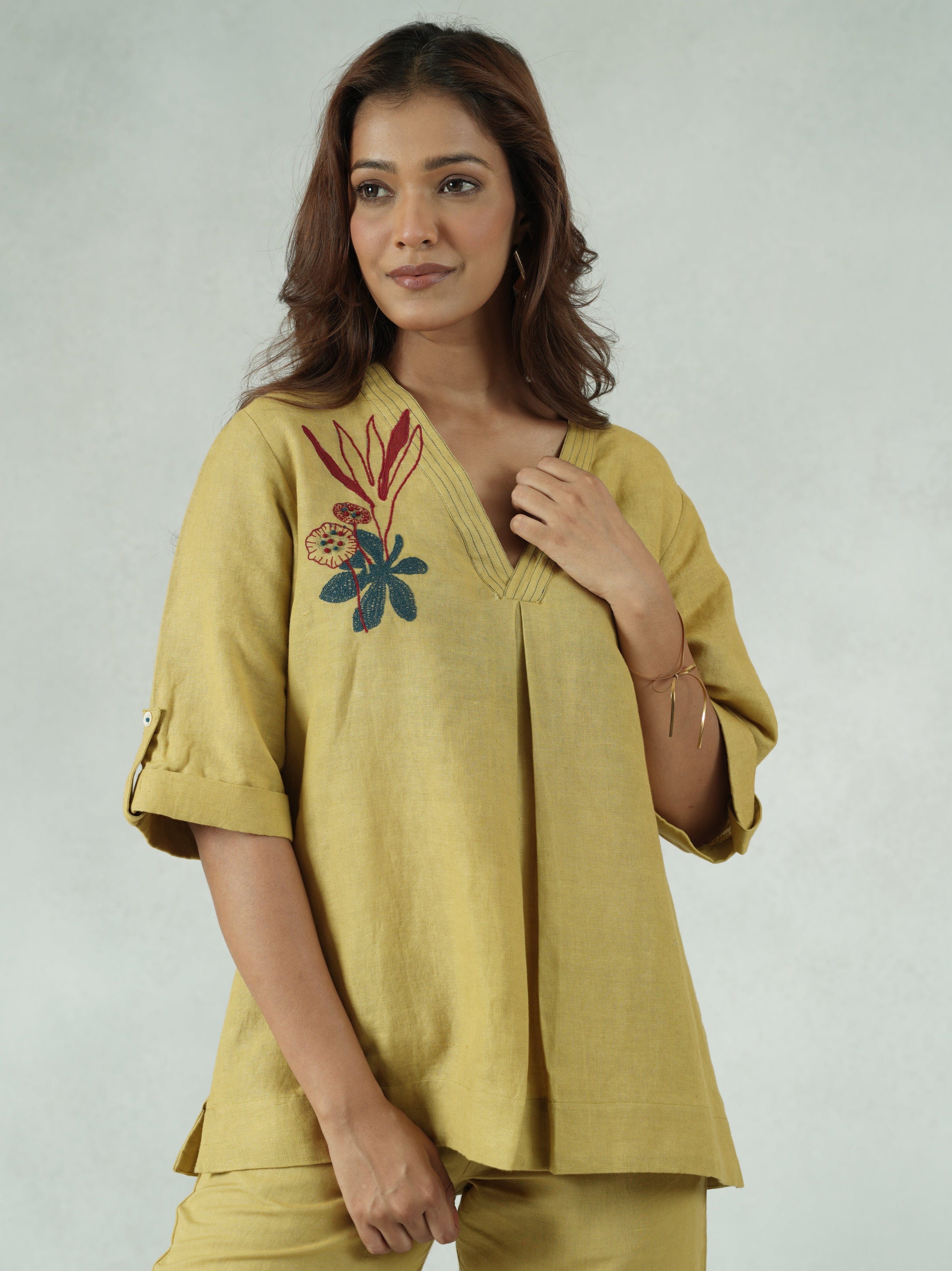 Woman wearing a yellow outfit with floral embroidery on a plain background