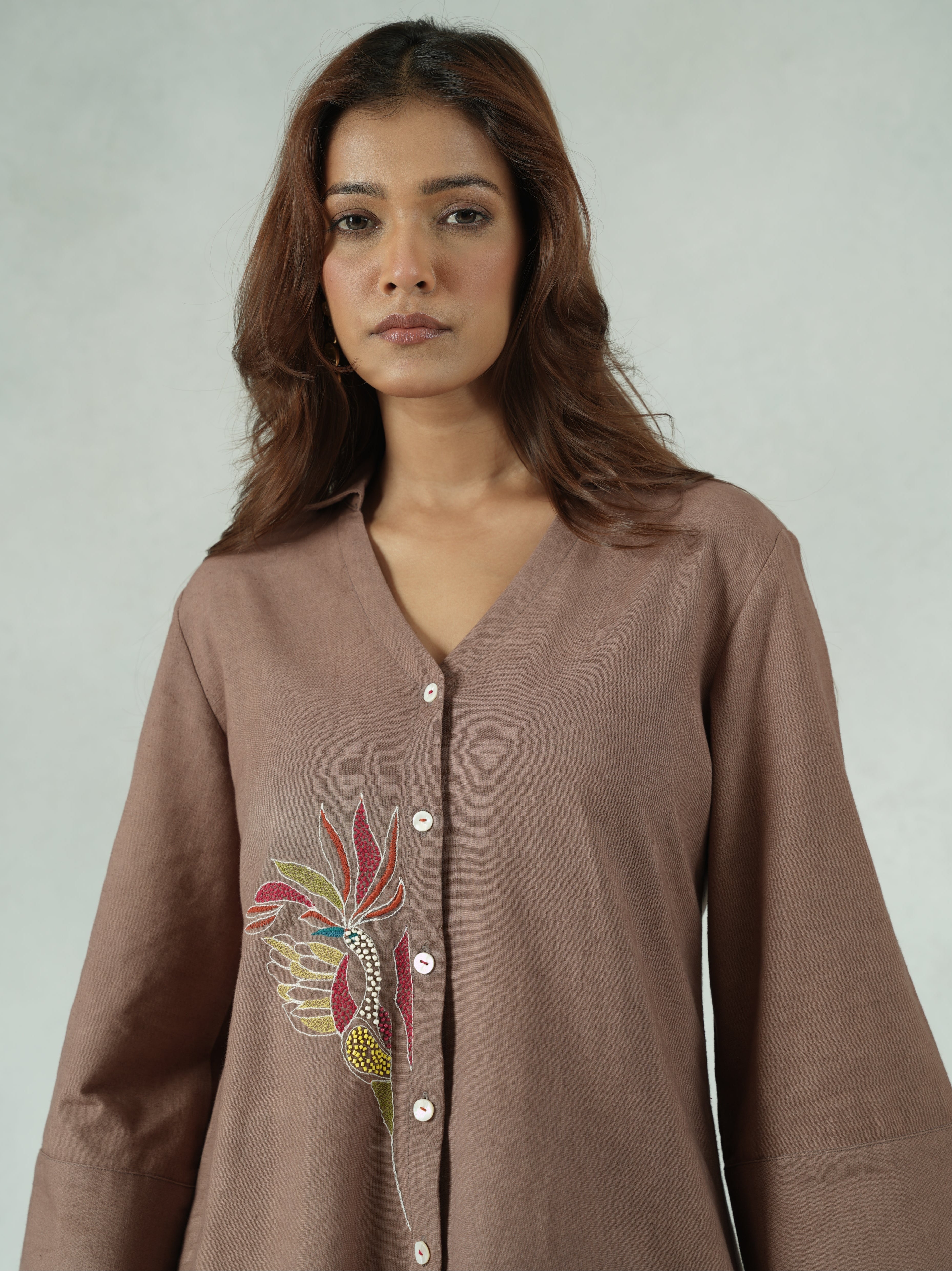 Woman wearing a brown embroidered dress against a plain background
