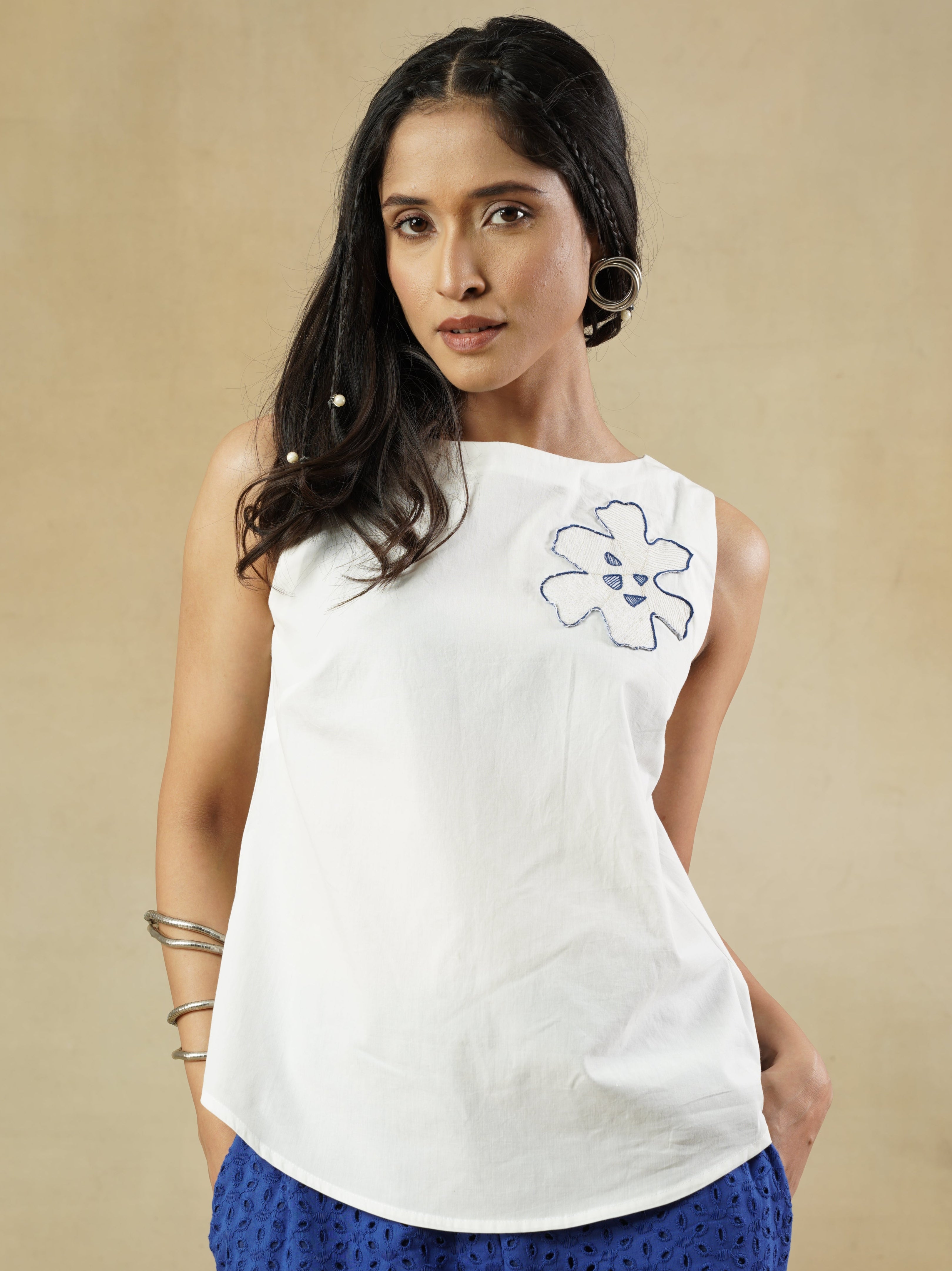 Woman wearing a white top with a floral design and blue skirt on a beige background