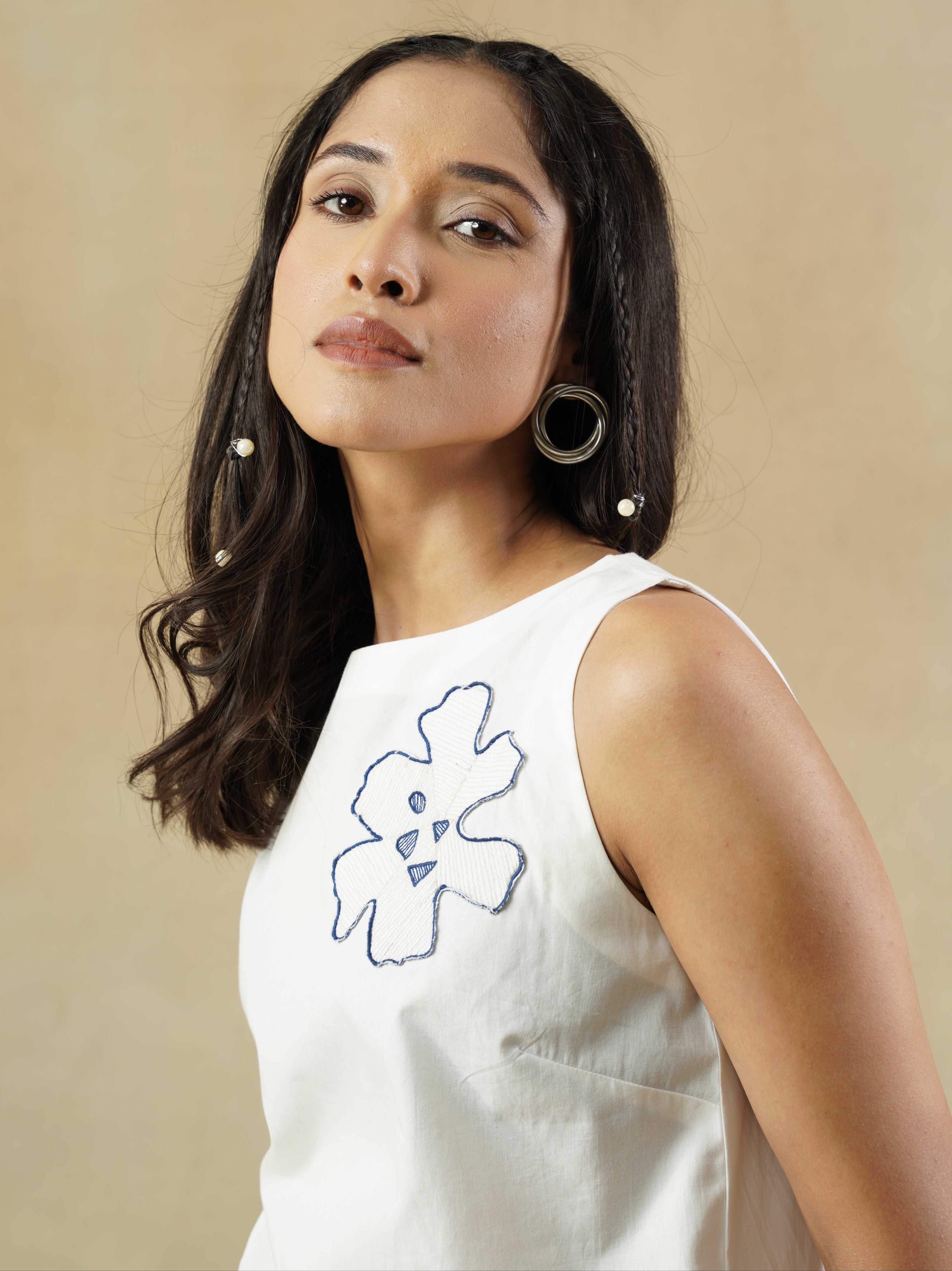 Woman wearing a white sleeveless top with a blue design on a beige background