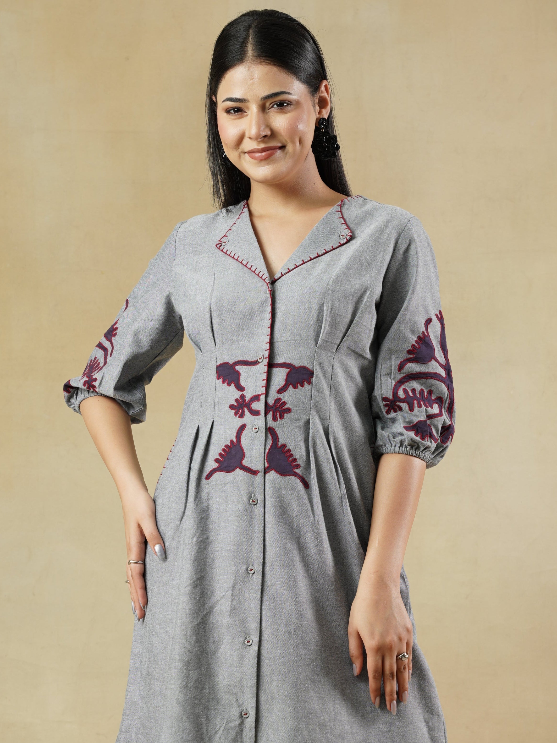 Woman wearing a gray dress with floral embroidery on a beige background