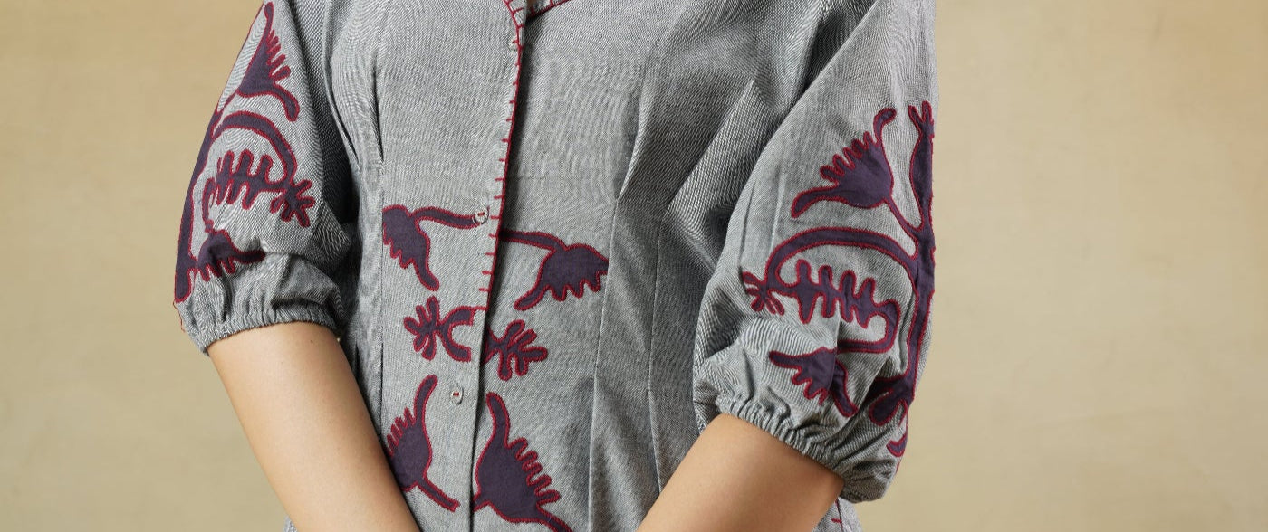 Woman wearing a gray outfit with red floral embroidery on a beige background