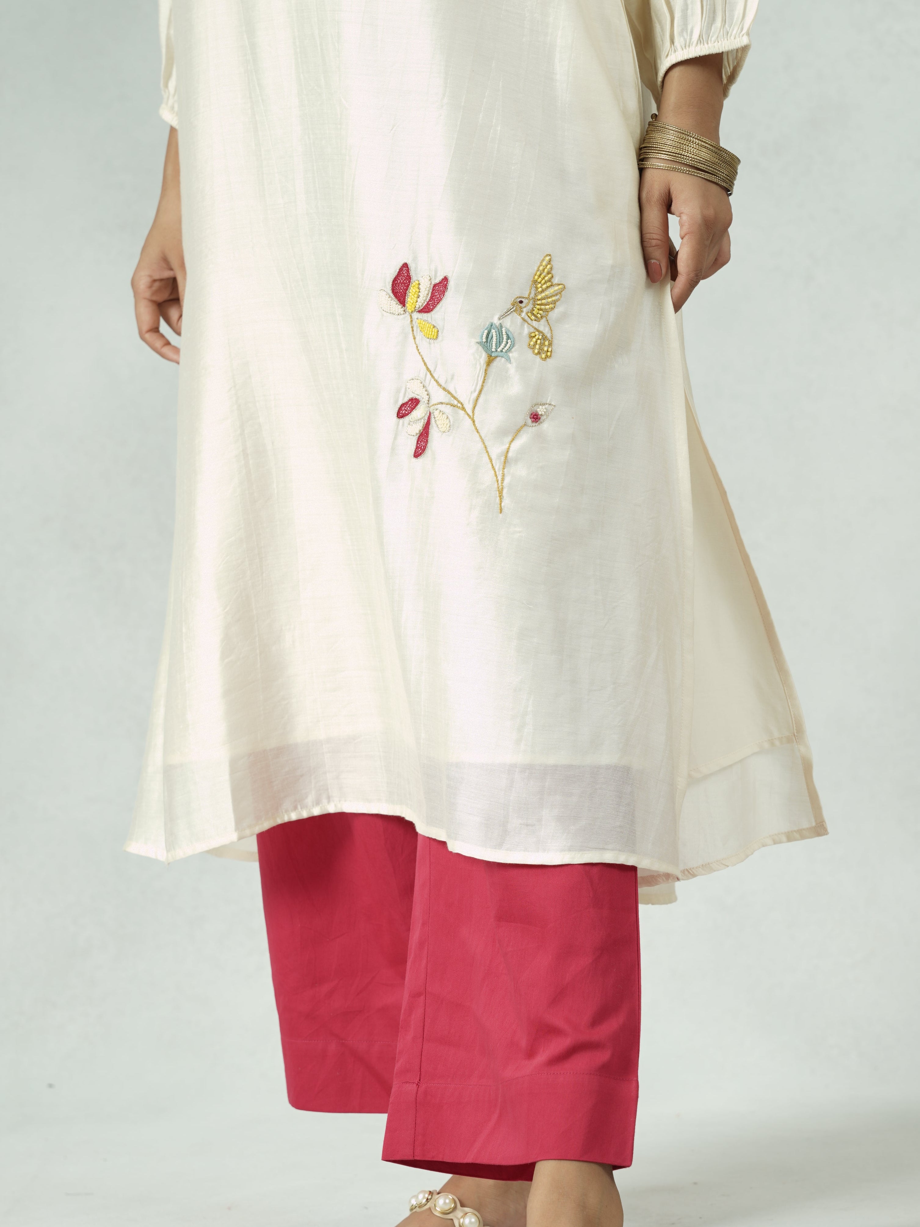 Person wearing a white outfit with red pants and gold sandals on a plain background