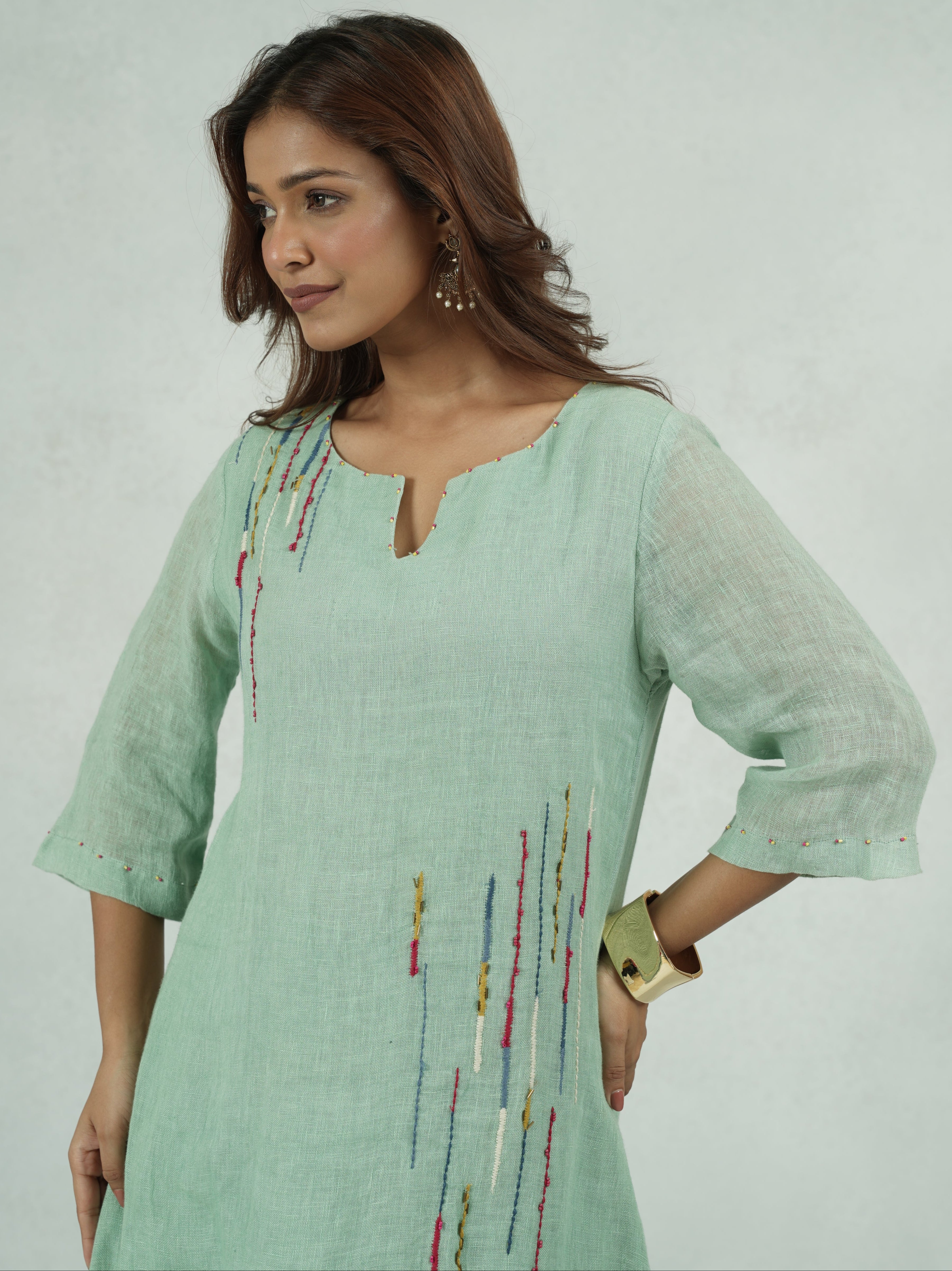 Woman wearing a light green traditional outfit with intricate patterns on a white background