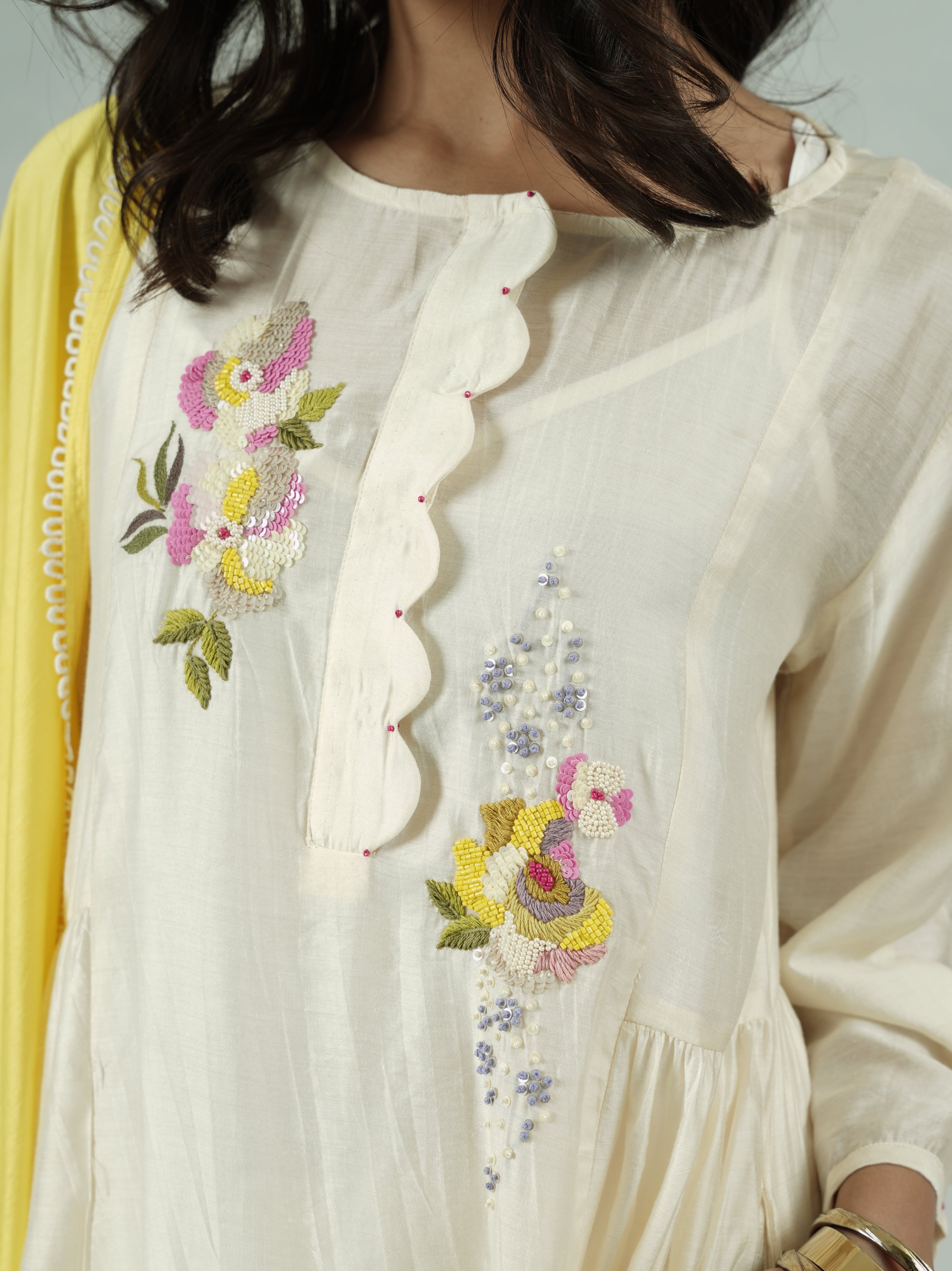 Close-up of a white garment with floral embroidery, worn by a person.