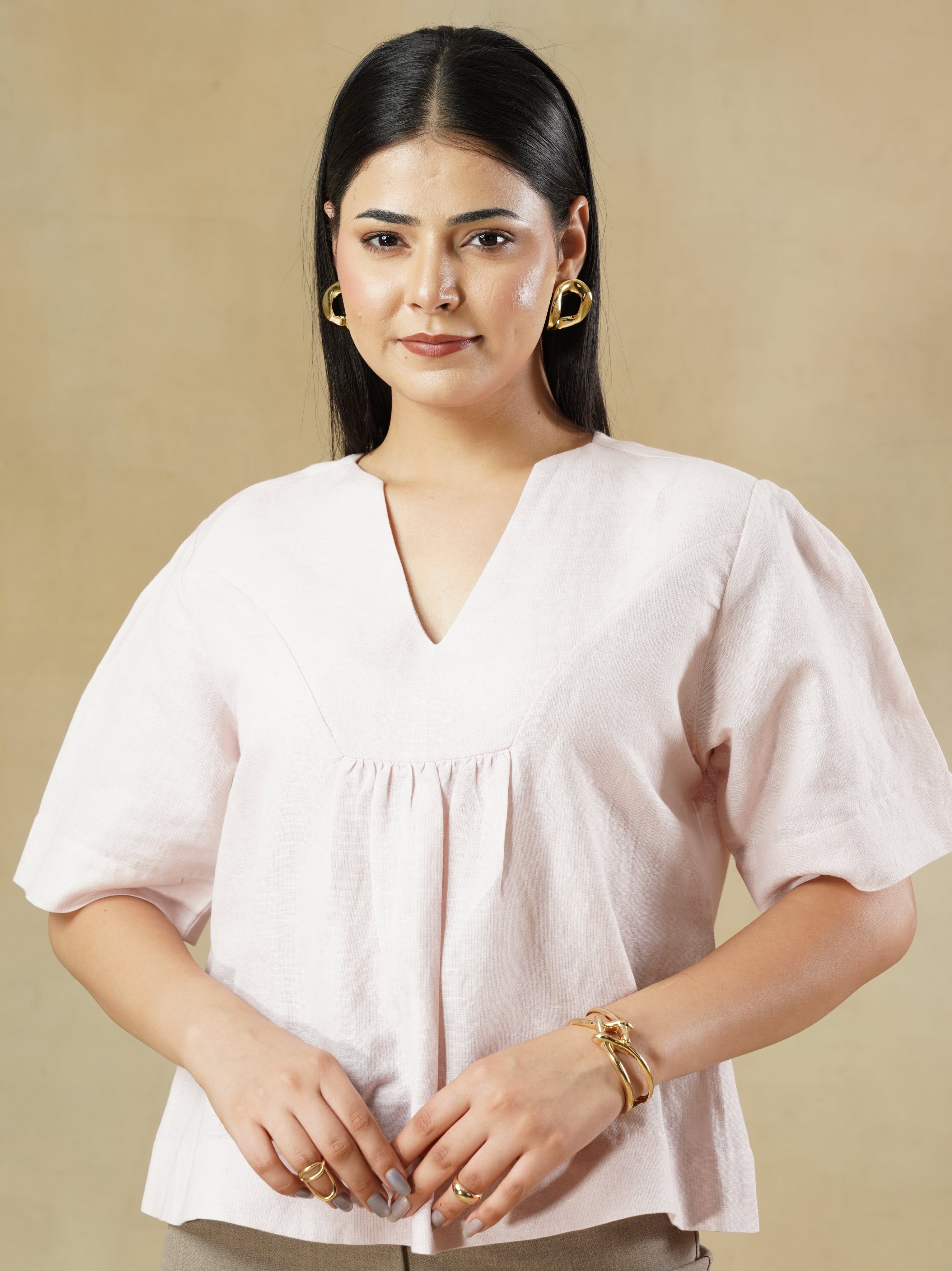 Woman wearing a white blouse and beige pants against a beige background