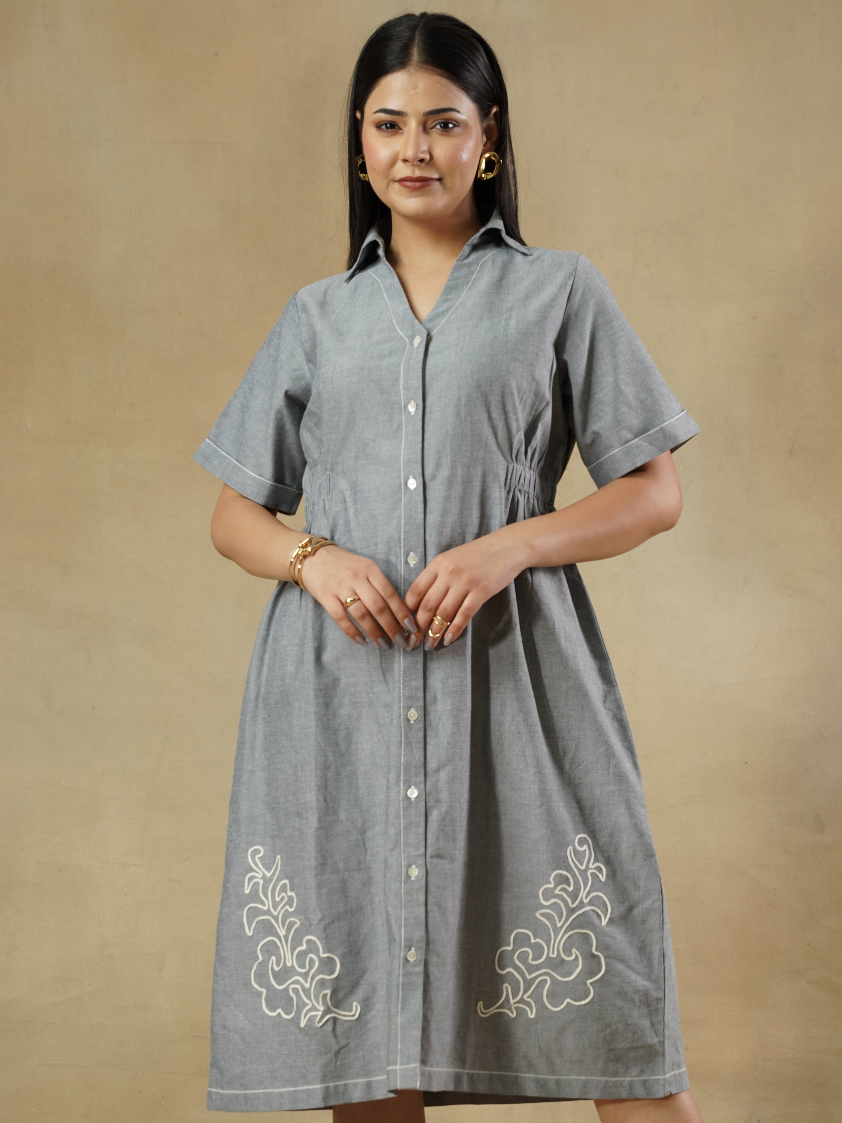 Woman wearing a gray dress with white embroidery on a beige background